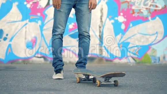 一个年轻人站在涂鸦墙边抬着滑板视频的预览图