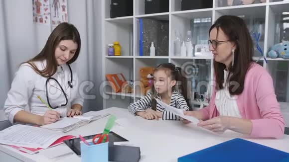 儿童医生给一个小女孩开维他命药她和母亲一起到一家诊所接待客人视频的预览图