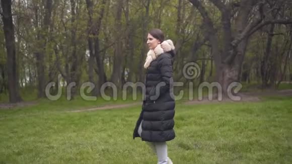 一个穿着暖和的黑色夹克的女孩穿过树林女孩和照相机在平行移动视频的预览图