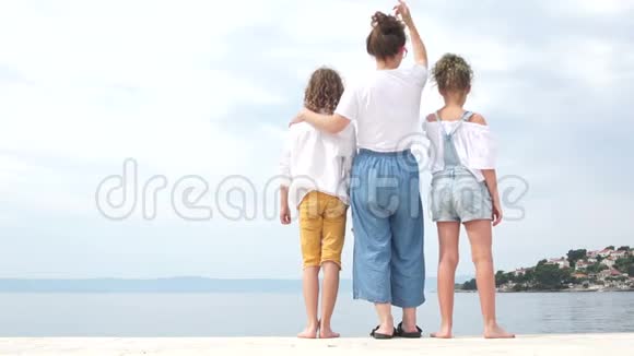 家庭假期快乐母亲节穿着牛仔布蓝色牛仔裤妈妈和她的两个十几岁的孩子站在岸边视频的预览图