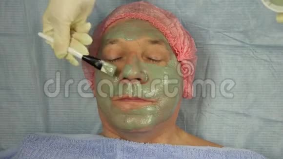 一位戴手套的男性美容师用特殊的刷子在客户的脸上了一个泥面具视频的预览图