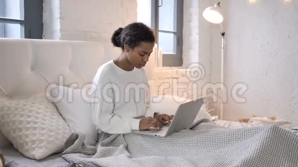 疲惫的非洲女孩颈部疼痛在床上做笔记本电脑视频的预览图
