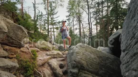 一个背着背包的女人站在森林里的巨大石头上散步和积极的生活方式视频的预览图