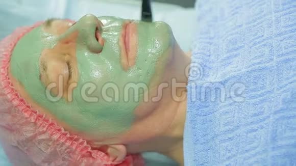 一位女性美容师用刷子把一个治愈泥面具涂在男人的脸上侧视图视频的预览图
