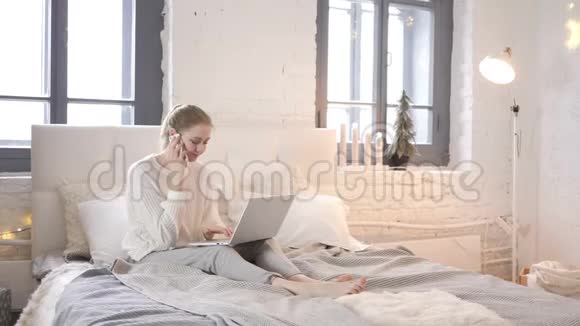 坐在床上和使用笔记本电脑的女孩在电话上交谈视频的预览图