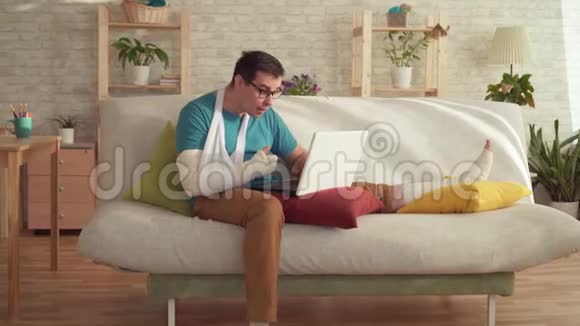 一个胳膊和腿断了的年轻人用笔记本电脑学习胜利视频的预览图
