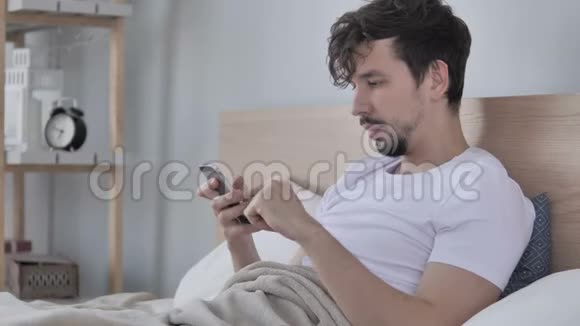 休闲青年在床上使用智能手机庆祝成功视频的预览图