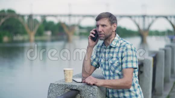 成熟的男人在河边码头用手机聊天视频的预览图