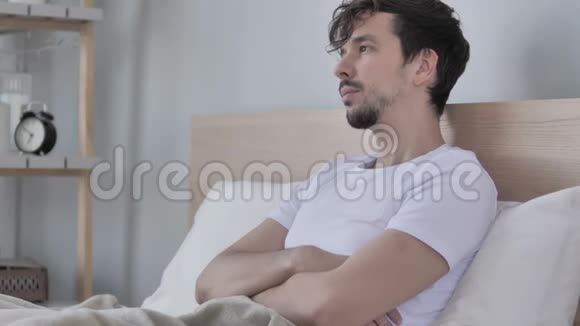 有头痛的疲惫的年轻休闲男子坐在床上视频的预览图
