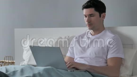 头痛紧张的年轻人在床上工作视频的预览图