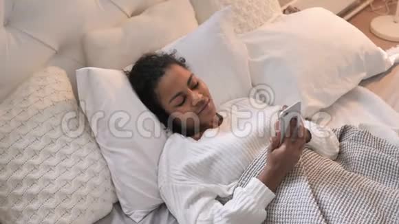 非洲女孩在床上放松时使用智能手机的最佳视角视频的预览图