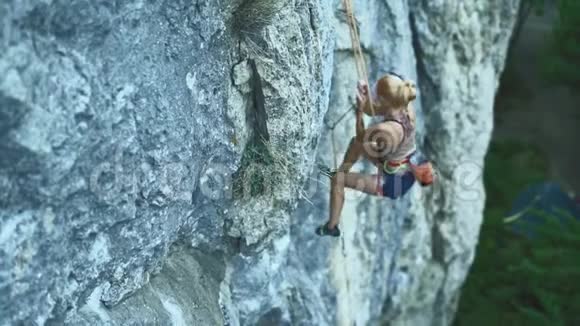 女子攀岩者挂在一根绳子上在艰难的运动路线上休息和粉笔手视频的预览图