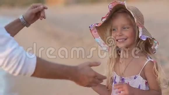 父亲慢慢地在海上捡起戴帽子的小女孩视频的预览图