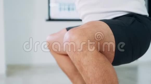 人用水壶铃做蹲式动作工作室里的一个人举起重物做一个蹲穿短裤的男人双腿合拢视频的预览图