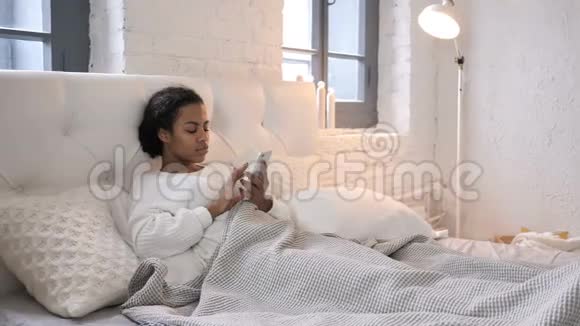 年轻的非洲女孩在床上使用智能手机庆祝成功视频的预览图