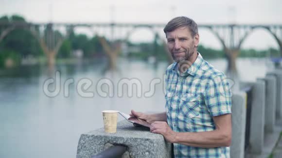 夏天成熟的男人在河边的码头上浏览数字平板电脑视频的预览图
