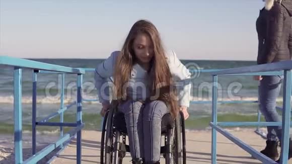 坐在轮椅上的残疾青年妇女正在靠近海边的坡道旁为残疾人滚动视频的预览图
