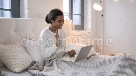 坐在床上的非洲少女在笔记本电脑上的在线视频聊天视频的预览图