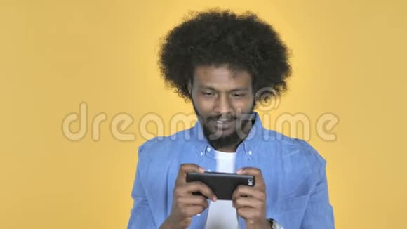 非裔美国人在黄色背景下玩智能手机游戏视频的预览图