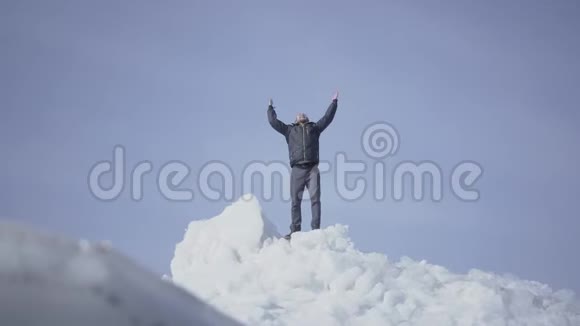 情绪愉快的男人穿着温暖的外套站在冰川顶部举起双手凯旋而归令人惊叹的景色视频的预览图
