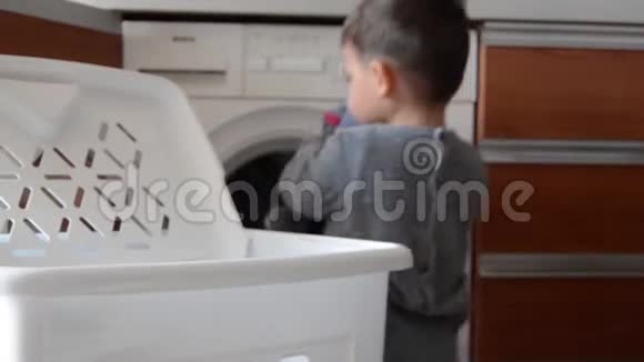 可爱的两岁男孩穿着睡衣帮忙洗衣服把鞋子放进洗衣机专注于洗衣视频的预览图