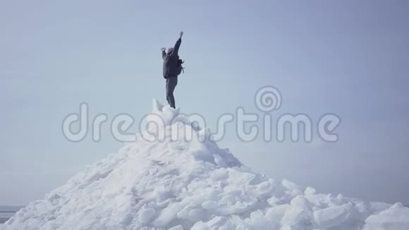 情绪愉快的男人穿着温暖的外套站在冰川顶部举起双手凯旋而归令人惊叹的景色视频的预览图
