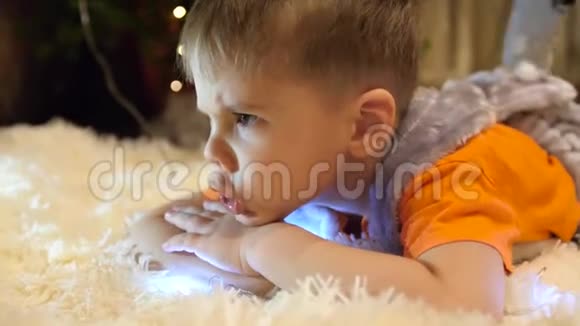 孩子在孩子们房间里玩圣诞灯他躺在柔软的毯子上做脸快乐视频的预览图