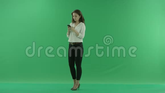 穿着休闲服的严肃漂亮的年轻女子正站在绿色面前的手机上聊天视频的预览图