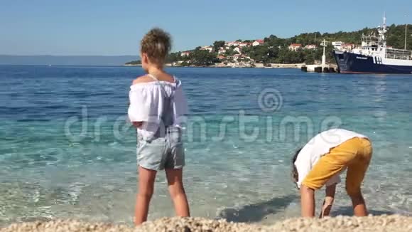 一个男孩和一个女孩的学童男孩和一个女孩在清澈的绿松石清澈的海水中扔石头视频的预览图