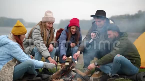 饥肠辘辘的旅行者正在火上煮棉花糖在篝火旁谈话时用棍子吃棉花糖视频的预览图