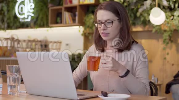 工作妇女在桌旁浏览笔记本电脑和喝茶视频的预览图