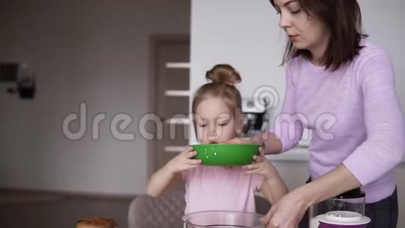 年轻的母亲和女儿穿着家庭服装在一个真正明亮的厨房里做煎饼面团从黄色中倒入牛奶视频的预览图