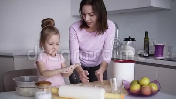 快乐的母亲和她的孩子一个女孩在他们现代的白色厨房准备蛋糕时玩得很开心他们玩视频的预览图