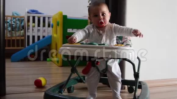 可爱的六个月大的男婴在老婴儿步行者中来回走动做出滑稽的面部表情视频的预览图