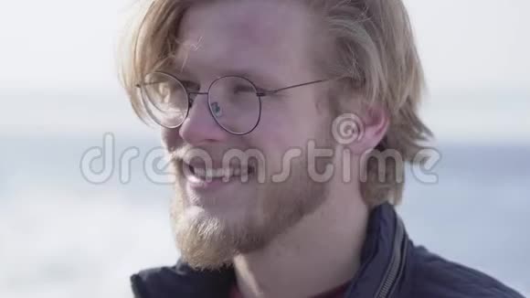 一个戴着金色头发的眼镜长着胡须的英俊男子的特写肖像在镜头中微笑着看着户外休闲视频的预览图