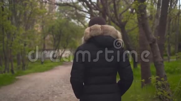 一个穿着暖和的黑色夹克的女孩穿过树林女孩走到前面镜头跟着她视频的预览图