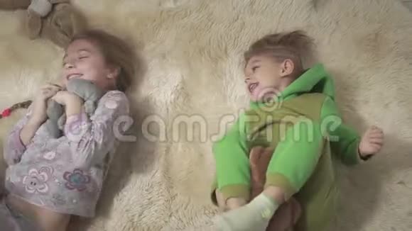 两个可爱的孩子在蓬松的地毯上滚动兄弟姐妹玩得开心孩子们周末快乐视频的预览图