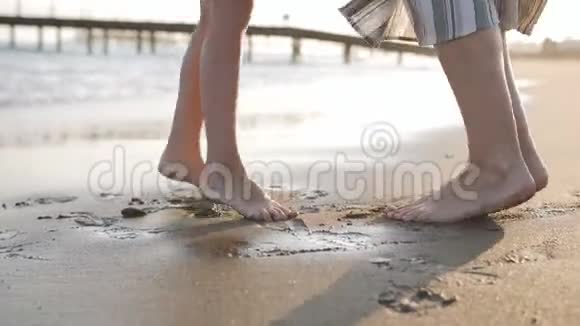 日落时分在海边的沙滩上妈妈和小女儿的双脚特写幸福的家庭视频的预览图