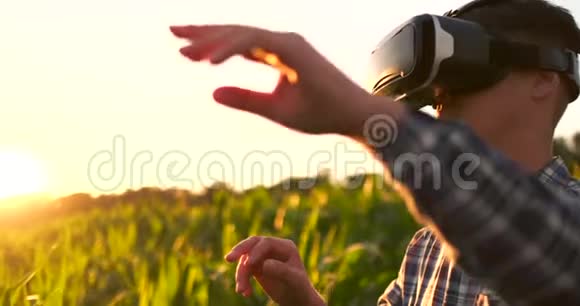 现代农民在VR头盔控制玉米作物站在田野日落阳光视频的预览图