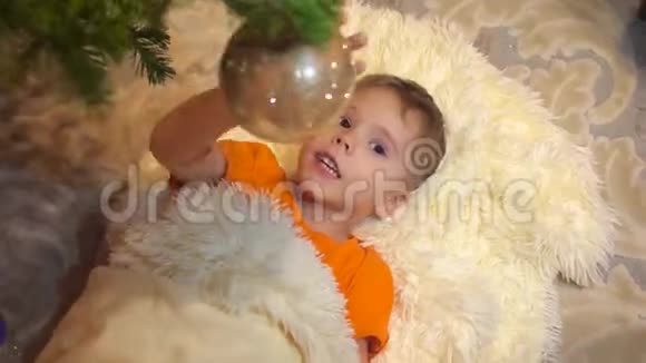 孩子在孩子们房间里玩圣诞树那个男孩躺在一条白色的蓬松毯子上快乐的童年视频的预览图