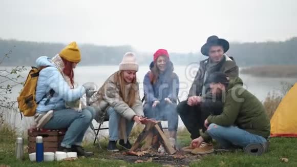 饥肠辘辘的旅行者正在火上煮棉花糖在篝火旁谈话时用棍子吃棉花糖视频的预览图
