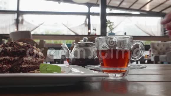 从咖啡桌上的透明茶壶中在玻璃杯中倒入丰富的茶木桌上的茶杯和巧克力派视频的预览图