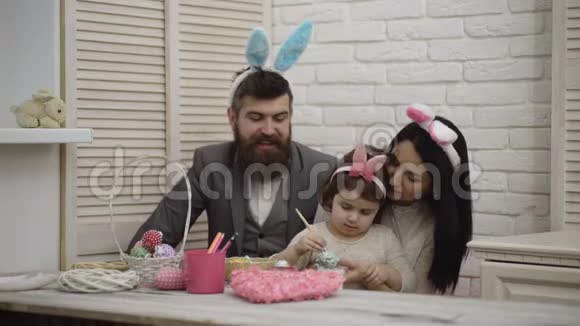 母亲父亲和女儿正在画复活节彩蛋幸福的家庭正在为复活节做准备可爱的小女孩视频的预览图
