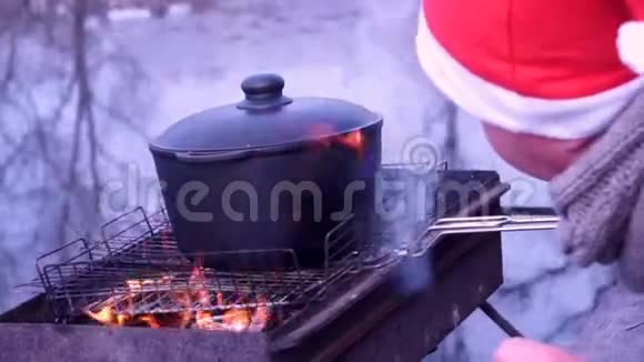 火上皮拉夫的准备煮汤大自然河流早晨冷酷戴圣诞老人帽子的人视频的预览图