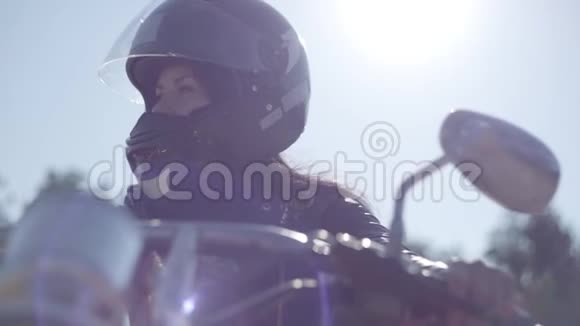 肖像可爱的女孩戴着黑色头盔坐在摩托车上看着远处爱好旅游和积极的生活方式视频的预览图