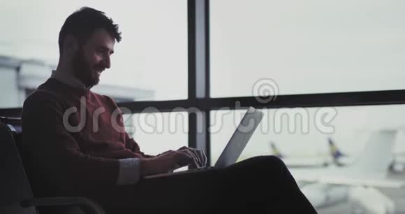 一个年轻人在机场候机区用笔记本电脑工作的画像然后他关上笔记本电脑走向视频的预览图