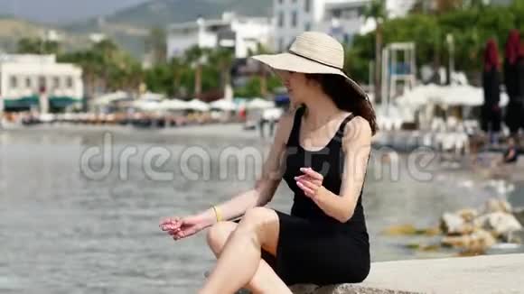 穿着黑裙子戴圆帽子的可怜的漂亮女人坐在港口做梦视频的预览图