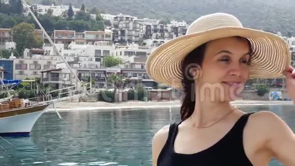 戴着圆夏帽的漂亮女孩欣赏度假小镇的景色在港口停泊的游艇和船只视频的预览图