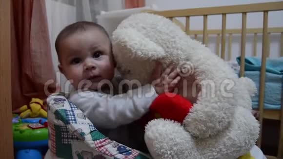 可爱的六个月大的男婴在步行者拿着白色的大玩具熊亲吻他拉他的耳朵视频的预览图