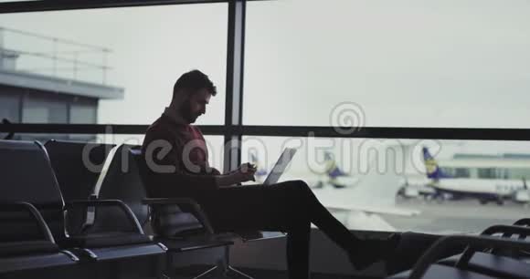 在机场等候区微笑的男人用他的笔记本和银行卡在网上下订单直到他等待视频的预览图